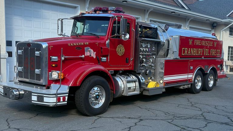 A large red fire rescue tanker truck labeled "Crabrun Vol. Fire Co." is parked on a driveway in front of a garage. The truck features chrome details, equipment panels, and an American flag decal.